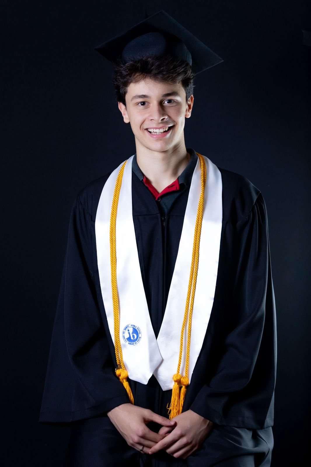 Enzo in his graduation cap and gown, wearing the IB Diploma stole